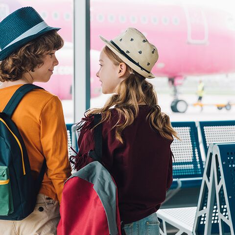 Kinderen voor een vliegtuig, die wachten om op reis te gaan