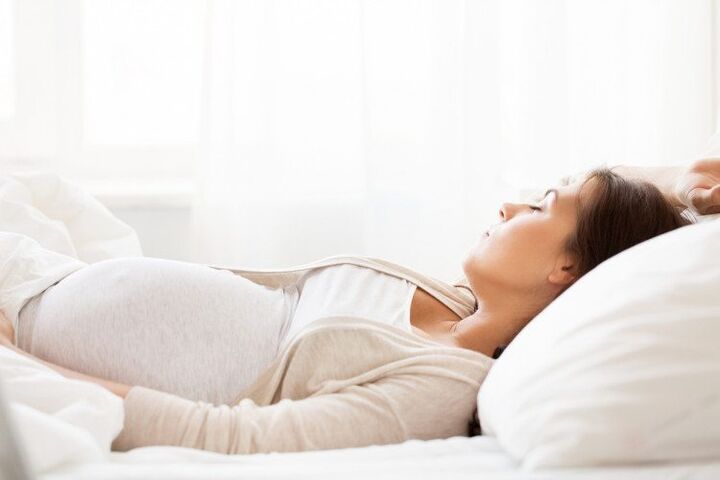 Vrouw die zwanger is ligt te rusten op bed na zwangerschapsvergiftiging