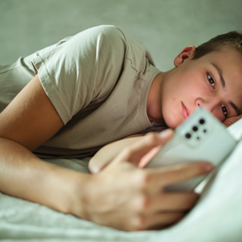 tiener die op bed ligt met een telefoon in zijn hand