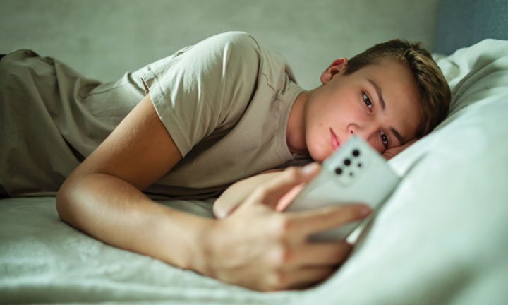 tiener die op bed ligt met een telefoon in zijn hand